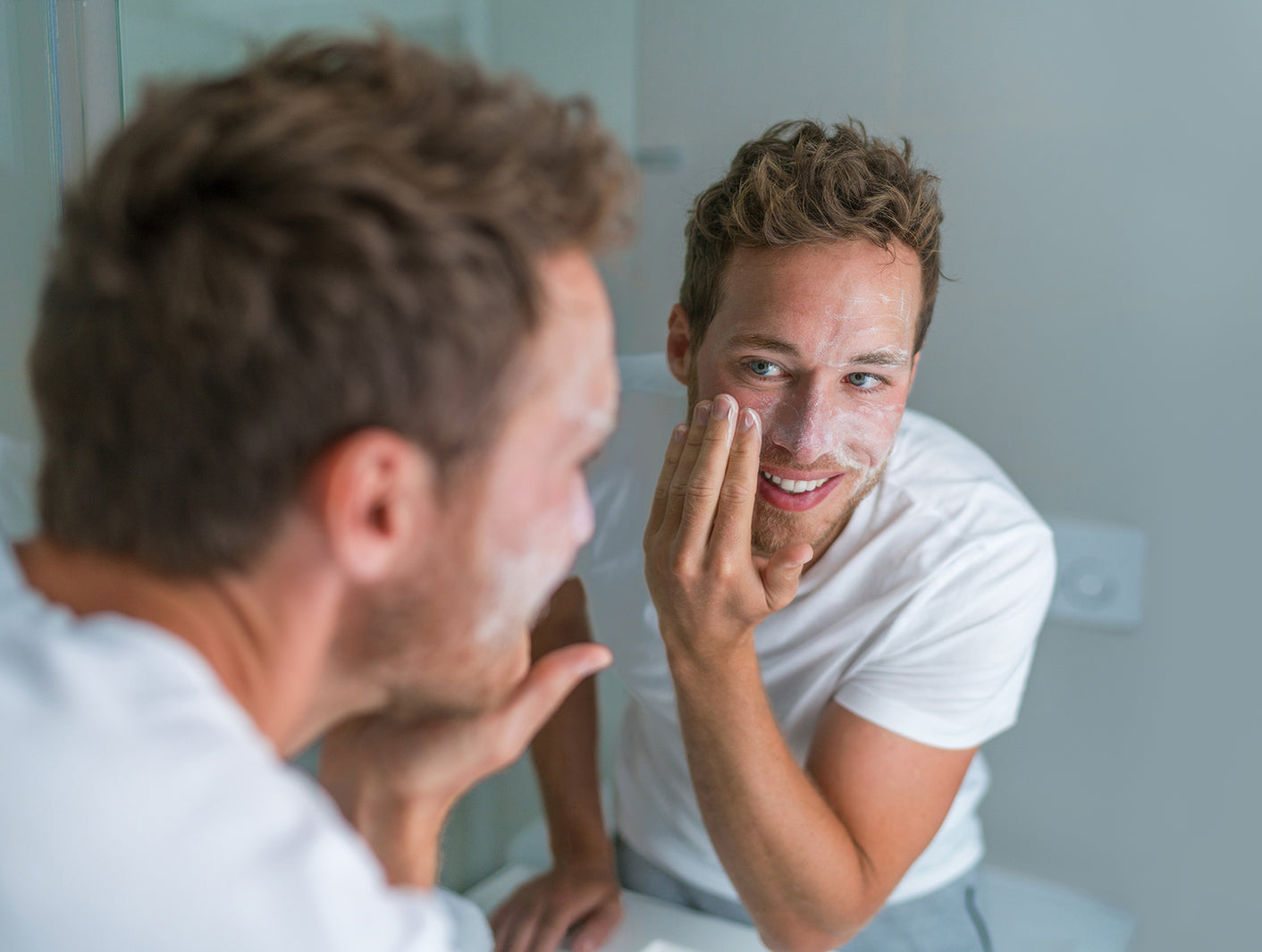 A close-up image of a man applying a moisturizer in front of a mirror, showcasing a simple and effective male skincare routine.