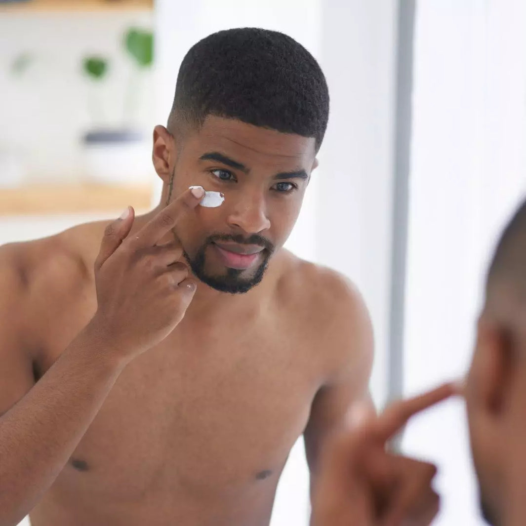 A person applying a skincare serum in front of a bathroom mirror, symbolizing a daily skincare routine.