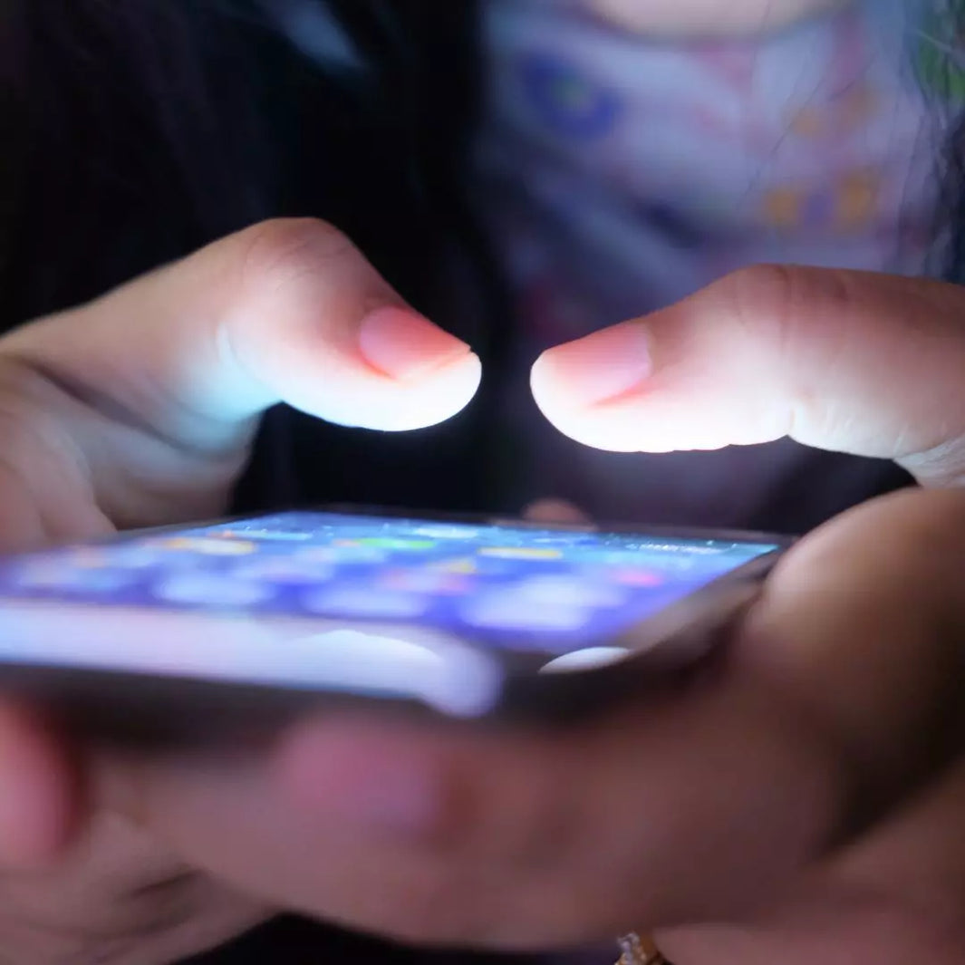 An image showing a person looking at their smartphone or laptop, with subtle visual effects of blue light emitting from the device and highlighting the skin. Blue Light and Your Skin: How Screen Time is Accelerating Aging